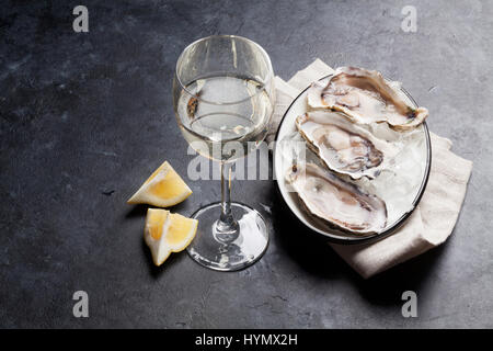 Geöffnete Austern, Eis und Zitrone und Weißwein auf steinernen Tisch. Selektiven Fokus auf Austern Stockfoto