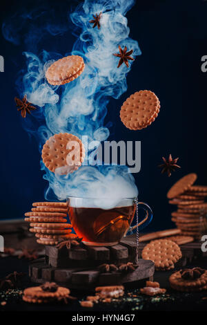 Dampfende Tasse Tee mit fliegenden Kekse und Gewürze Stockfoto