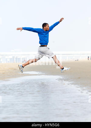 Junger sportlicher Mann laufen und springen am Strand Stockfoto