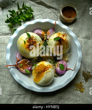 Große weiße Zwiebeln, Schalotten und Knoblauch in weiß Bräter mit Kräutern und Gewürzen auf Tisch mit Sackleinen Tuch in weiches Licht Stockfoto