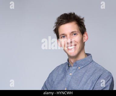 Porträt eines lächelnden jungen Mannes posiert vor grauem Hintergrund hautnah Stockfoto