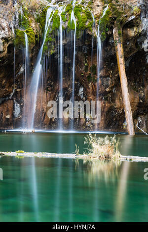 Eine Langzeitbelichtung glättet die Gewässer der Bridal Veil Falls oben Hanging Lake und verwischt das Unkraut auf einem Baumstamm in den See. Das Wasser im See ist Stockfoto