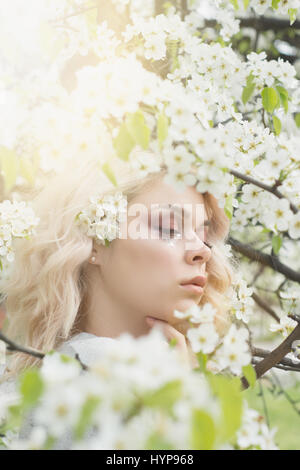 Schönes Mädchen mit blonden Locken im Frühling Blumengarten, klare gute warme Tag. Frühlingszeit. Stockfoto