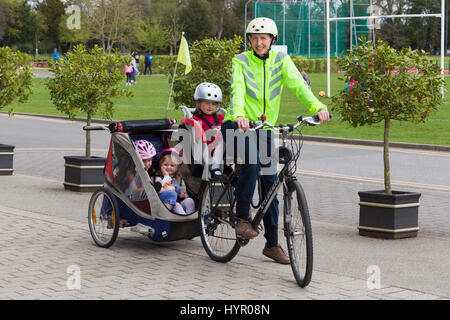 Frau Radfahrer auf Bike / Fahrrad mit + 3 Kinder; Co-Pilot Kindersitz mit Helm & Abschleppen Zyklus Chariot Anhänger mit zwei / 2 Kinder mit Helmen. VEREINIGTES KÖNIGREICH. Stockfoto