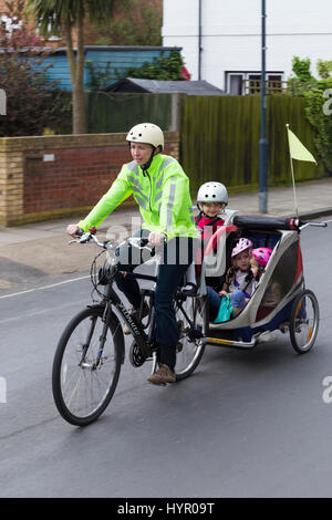 Frau Radfahrer auf Bike / Fahrrad mit + 3 Kinder; Co-Pilot Kindersitz mit Helm & Abschleppen Zyklus Chariot Anhänger mit zwei / 2 Kinder mit Helmen. VEREINIGTES KÖNIGREICH. Stockfoto