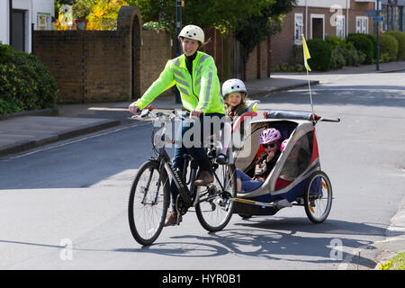 Frau Radfahrer auf Bike / Fahrrad mit + 3 Kinder; Co-Pilot Kindersitz mit Helm & Abschleppen Zyklus Chariot Anhänger mit zwei / 2 Kinder mit Helmen. VEREINIGTES KÖNIGREICH. Stockfoto