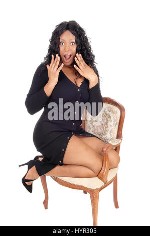Eine Nahaufnahme Bild einer sehr überrascht afroamerikanische Frau mit großen Augen und offenem Mund kniend im Sessel, für weißen Hintergrund isoliert. Stockfoto