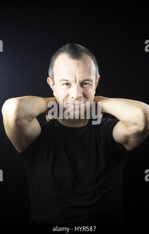 Attraktive hübscher schlanke gesunde Mann im Alter von in 40er Jahren in schwarzes T-shirt gegen schlicht schwarz Studio Portrait-Hintergrund. Stockfoto