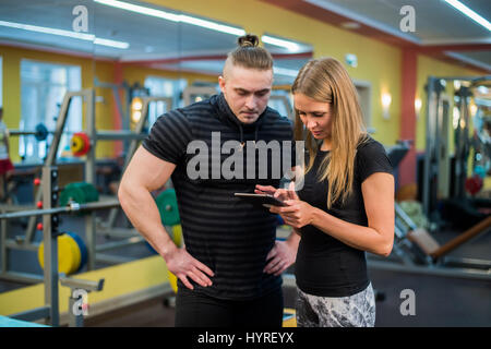 Passen Sie attraktives junges Paar in einem Fitnessstudio, einem Tablet-pc zu betrachten, wie sie ihre Fortschritte und Fitness überwachen Stockfoto