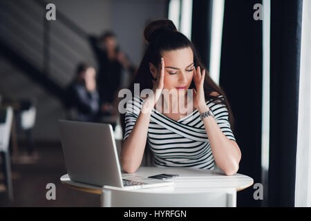 Frau sitzt in einem Café vor einen Laptop zu denken ein Problem mit ihren Händen berühren Kopf. Erwachsenen Dame versucht, eine Lösung zu finden. Stockfoto