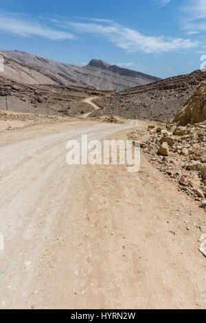 Vertikaler Blick auf eine unbefestigte Straße, die sich durch zerklüftete, wilde Berge der Arabischen Halbinsel schlängelt, bietet eine malerische Aussicht mit blauem Himmel, Kopierraum Stockfoto