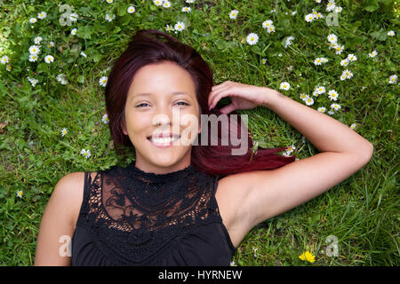 Porträt einer schönen Mischlinge Frau liegend auf dem Rasen und lächelnd hautnah Stockfoto