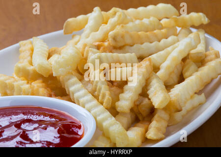 Ein Teller voll mit leckeren Crinkle cut Stil Pommes Frites mit ketchup Stockfoto