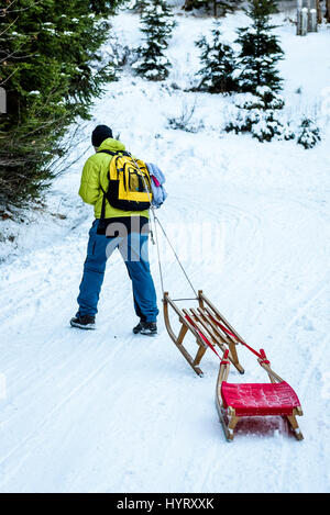 Person zieht Schlitten auf der Bergstrasse in Wäldern. Aktive Menschen in den Wintersport-Aktivitäten mit Schlitten an verschneiten Waldweg gleiten. Stockfoto