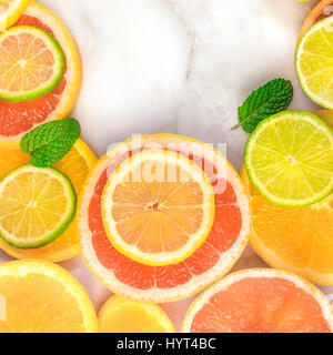 Ein quadratischer Rahmen, bestehend aus saftigen Zitrusfrüchten, auf eine weiße Marmor Textur mit Textfreiraum. Grapefruit, Limone, Zitrone und Orange Scheiben mit Minze Stockfoto