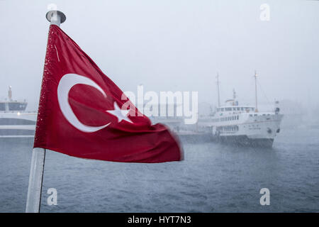 ISTANBUL, Türkei - 30. Dezember 2015: Türkische Flagge während eines Schneesturms, einer Europa-Asien-Fähre im Hintergrund Bild von Schiffen auf Euro ersichtlich Stockfoto