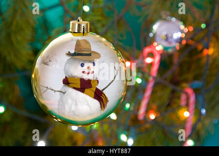 Ein Bsnowman spiegelt sich in einem Weihnachtsbaum Ornament mit Zuckerstangen und Lichter auf einen Weihnachtsbaum. Stockfoto