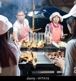 Quadratische Porträt des Kunden kaufen BBQ'd Fleischspieße auf einem Straßenmarkt in Kambodscha Stockfoto