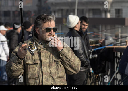 ISTANBUL, Türkei - 27. Dezember 2015: Fischer am Galata-Brücke, eine Zigarette rauchen, bevor ab Bild von einem mittleren Fischen Vorbereitung t Mann im Alter von Stockfoto