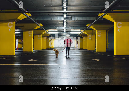 Mädchen mit weißem Hut und rote Jacke, die zu Fuß in der öffentlichen Garage mit kleinen gelben Hund Stockfoto