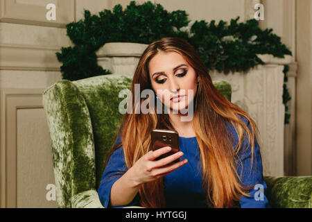 schönes junges Mädchen in einem Kleid mit Smartphone sitzt in einem Sessel. Horizontale Studio Foto Stockfoto