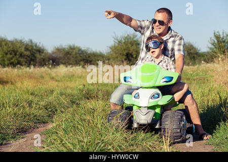 Vater und Sohn spielen auf der Straße an der Tageszeit. Sie fahren mit Quad im Park. Leute, die Spaß an der Natur. Konzept der freundlichen Familie Stockfoto