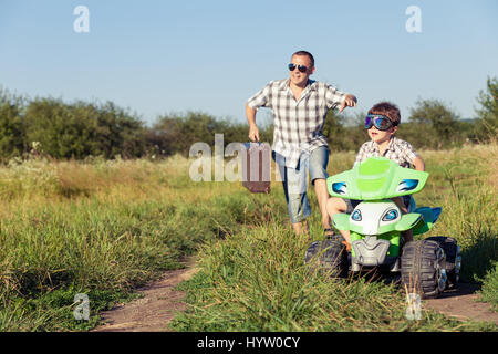 Vater und Sohn spielen auf der Straße an der Tageszeit. Sie fahren mit Quad im Park. Leute, die Spaß an der Natur. Konzept der freundlichen Familie Stockfoto