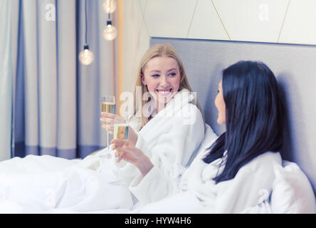 lächelnd Freundinnen mit Champagner Gläser im Bett Stockfoto