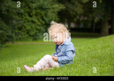 Porträt der ein kleines Mädchen sitzt auf dem grünen Rasen im freien Stockfoto