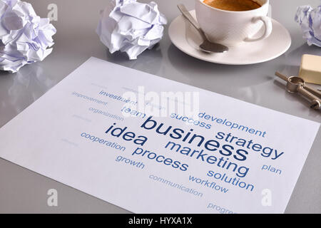 Konzept-Geschäft mit geschäftsrelevanten Wörter auf weißen Blatt auf grauen Bürotisch mit zerknitterten Laken und Kaffee im Hintergrund. Erhöhten Blick. H Stockfoto