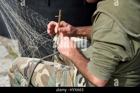 Hände bei der Arbeit am Fischernetz mit einem Werkzeug Stockfoto