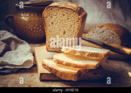 Sauerteig Brot Brot, in Scheiben geschnitten auf alten Holz Schneidebrett, Vintage Geschirr, Leinen Handtuch, authentischen ländlichen Stil, Stillleben, getönt Stockfoto