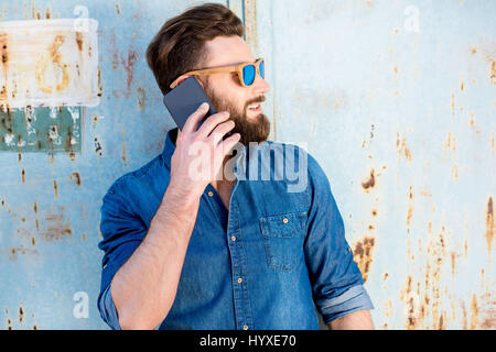 Gut aussehender Mann in blaues T-shirt mit Handy auf dem alten rostigen Wand-Hintergrund Stockfoto
