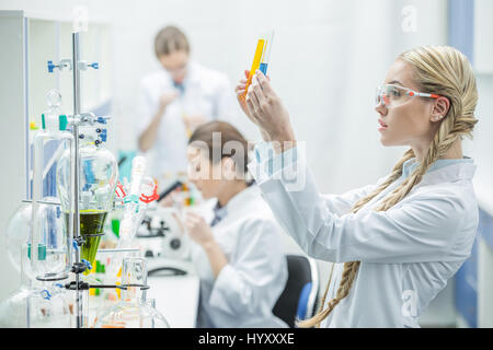 Junge Wissenschaftlerin betrachten Reagenzgläser mit chemische Proben im Labor Stockfoto