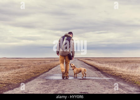 Wanderer und Hund zu Fuß hinunter eine Straße an einem bewölkten Tag Stockfoto