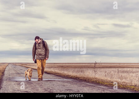 Wanderer und Hund zu Fuß hinunter eine Straße an einem bewölkten Tag Stockfoto