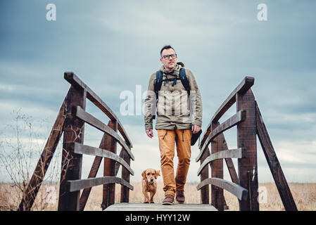 Wanderer und Hund überqueren Holzbrücke am bewölkten Tag Stockfoto