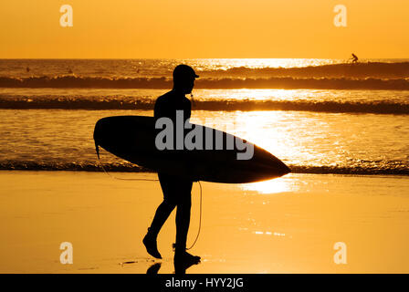 Surfer, die zu Fuß in den Sonnenuntergang am fistral Strand, Newquay, Cornwall, uk Stockfoto