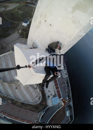 SEWASTOPOL, UKRAINE: Ein Adrenalin-Junkie hat Leib und Leben riskiert nach dem Klettern eines 195-Fuß hohe Denkmals für russische WW2 Kriegshelden nur um ein neues Video über die Stadt zu bekommen. Schwindelerregenden Bild- und Filmmaterial zeigen die furchtlosen Kletterer Bundle eine Leiter auf der Innenseite des Turms vor zu Fuß auf eine Oberfläche, die bei 45 Grad, ohne Sicherheitsausrüstung abgewinkelt ist. Der Rooftopper Spaziergänge auf die geneigte Fläche, bis er den Rand erreicht, wo er sitzt und seine Beine während beiläufig SMS auf seinem Handy baumelt. Das Herzschlagfinale Video wurde auf der Bajonett-Segel-Obelisk in Sevastopo gefilmt. Stockfoto