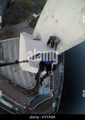 SEWASTOPOL, UKRAINE: Ein Adrenalin-Junkie hat Leib und Leben riskiert nach dem Klettern eines 195-Fuß hohe Denkmals für russische WW2 Kriegshelden nur um ein neues Video über die Stadt zu bekommen. Schwindelerregenden Bild- und Filmmaterial zeigen die furchtlosen Kletterer Bundle eine Leiter auf der Innenseite des Turms vor zu Fuß auf eine Oberfläche, die bei 45 Grad, ohne Sicherheitsausrüstung abgewinkelt ist. Der Rooftopper Spaziergänge auf die geneigte Fläche, bis er den Rand erreicht, wo er sitzt und seine Beine während beiläufig SMS auf seinem Handy baumelt. Das Herzschlagfinale Video wurde auf der Bajonett-Segel-Obelisk in Sevastopo gefilmt. Stockfoto