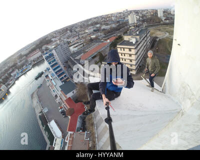 SEWASTOPOL, UKRAINE: Ein Adrenalin-Junkie hat Leib und Leben riskiert nach dem Klettern eines 195-Fuß hohe Denkmals für russische WW2 Kriegshelden nur um ein neues Video über die Stadt zu bekommen. Schwindelerregenden Bild- und Filmmaterial zeigen die furchtlosen Kletterer Bundle eine Leiter auf der Innenseite des Turms vor zu Fuß auf eine Oberfläche, die bei 45 Grad, ohne Sicherheitsausrüstung abgewinkelt ist. Der Rooftopper Spaziergänge auf die geneigte Fläche, bis er den Rand erreicht, wo er sitzt und seine Beine während beiläufig SMS auf seinem Handy baumelt. Das Herzschlagfinale Video wurde auf der Bajonett-Segel-Obelisk in Sevastopo gefilmt. Stockfoto