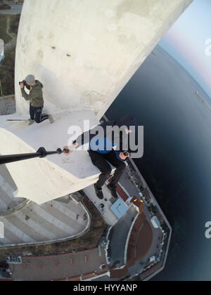 SEWASTOPOL, UKRAINE: Ein Adrenalin-Junkie hat Leib und Leben riskiert nach dem Klettern eines 195-Fuß hohe Denkmals für russische WW2 Kriegshelden nur um ein neues Video über die Stadt zu bekommen. Schwindelerregenden Bild- und Filmmaterial zeigen die furchtlosen Kletterer Bundle eine Leiter auf der Innenseite des Turms vor zu Fuß auf eine Oberfläche, die bei 45 Grad, ohne Sicherheitsausrüstung abgewinkelt ist. Der Rooftopper Spaziergänge auf die geneigte Fläche, bis er den Rand erreicht, wo er sitzt und seine Beine während beiläufig SMS auf seinem Handy baumelt. Das Herzschlagfinale Video wurde auf der Bajonett-Segel-Obelisk in Sevastopo gefilmt. Stockfoto