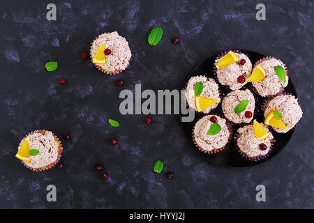 Zitronen-Cupcakes mit Kirsch Sahne. Cranberry, Minze Blätter. Essen auf einem dunklen Hintergrund. Ansicht von oben Stockfoto
