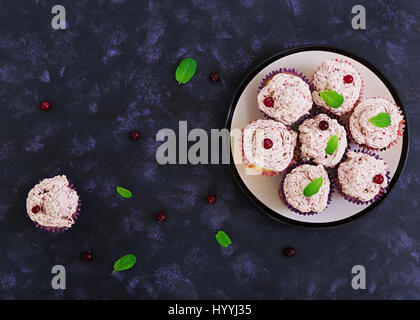 Zitronen-Cupcakes mit Kirsch Sahne. Cranberry, Minze Blätter. Essen auf einem dunklen Hintergrund. Ansicht von oben Stockfoto