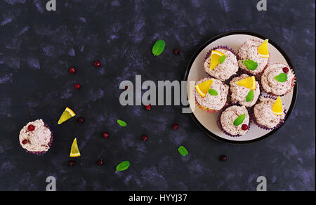 Zitronen-Cupcakes mit Kirsch Sahne. Cranberry, Minze Blätter. Essen auf einem dunklen Hintergrund. Ansicht von oben Stockfoto