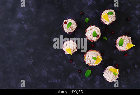 Zitronen-Cupcakes mit Kirsch Sahne. Cranberry, Minze Blätter. Essen auf einem dunklen Hintergrund. Ansicht von oben Stockfoto