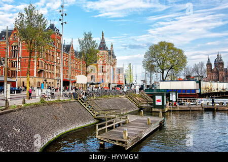 Amsterdam, Niederlande - 3. Mai 2013: Kanal auf offenen Havenfront in Amsterdam, Niederlande. Centraal Bahnhof und Menschen auf dem Hintergrund Stockfoto