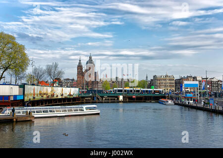 Amsterdam, Niederlande - 3. Mai 2013: Kanalboote und St. Nicholas Church in offenen Havenfront in Amsterdam, Niederlande. Menschen auf dem Hintergrund Stockfoto