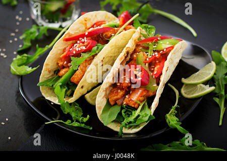 Mexikanische Tacos mit Hühnerfilet in Tomatensauce und Salsa von Paprika und Rucola Stockfoto