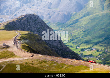 Ein Zug steigt Snowdon Mountain mit der Schmalspur-Zahnradbahn-Berg mit Llanberis Tal & Dinorwig Steinbruch hinter, in Snowdonia, Nordwales. Stockfoto